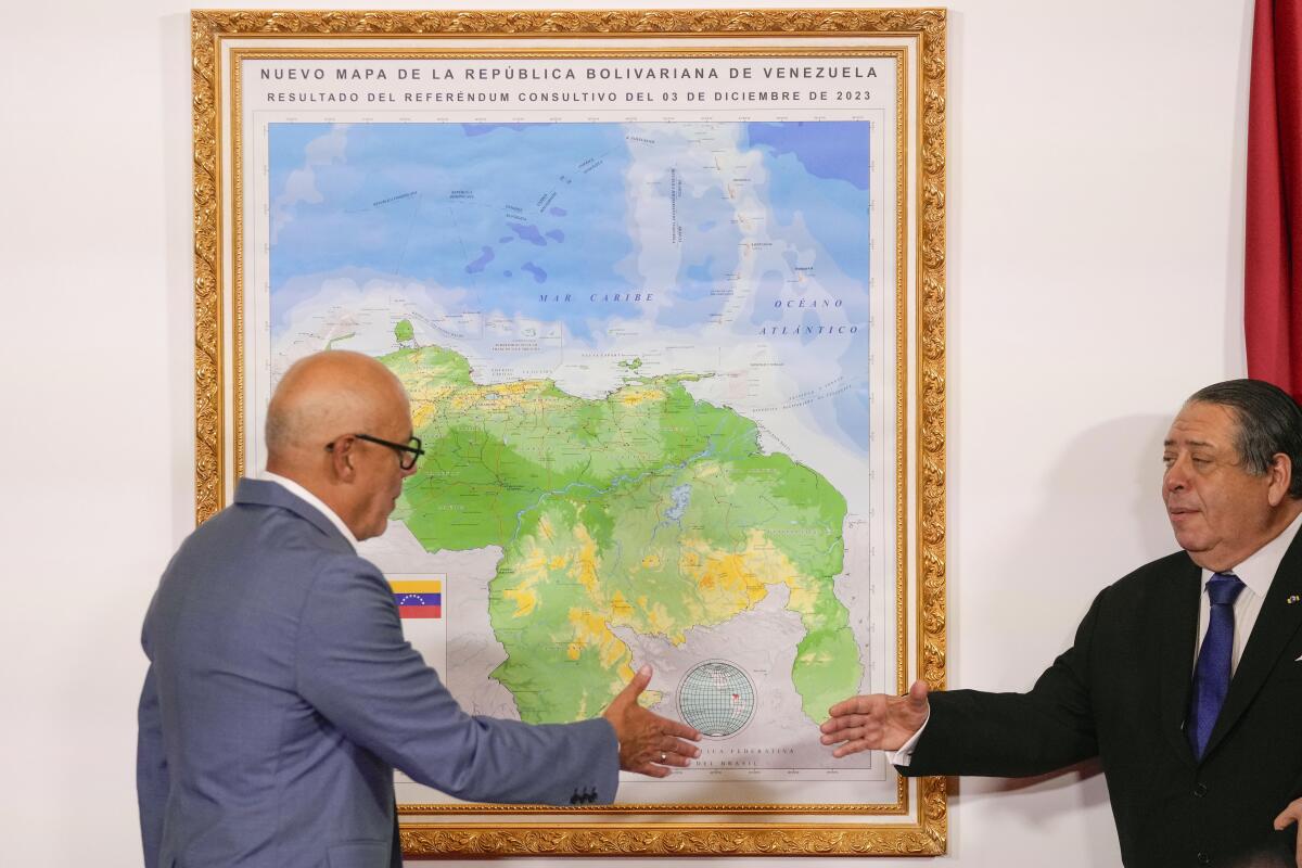 Two men in suits reach out to shake hands in front of a framed map. 