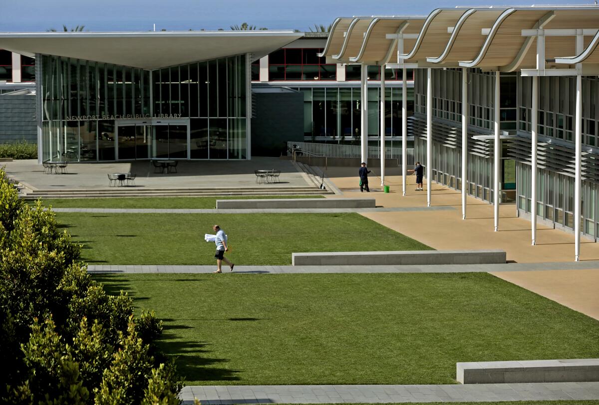 A pedestrian walks past the lawns between City Hall and the public library in Newport Beach.