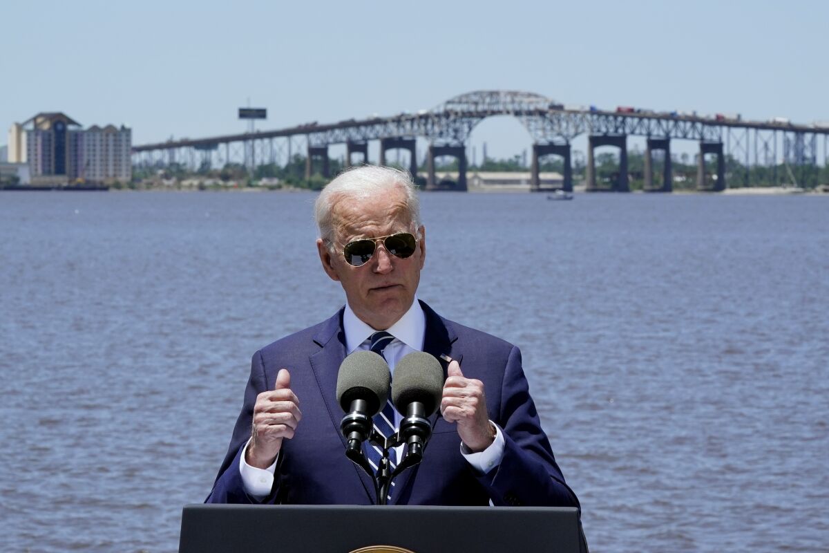 President Biden speaks in front of a lake and a large bridge.