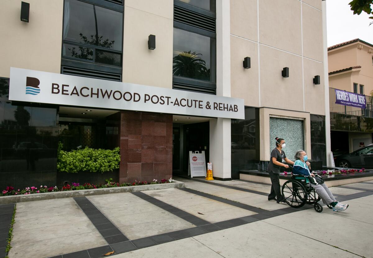 A worker pushes a resident in a wheelchair out of the Beachwood Post-Acute & Rehab center in Santa Monica on Monday. Beachwood has been cited for poor infection control the last three years.