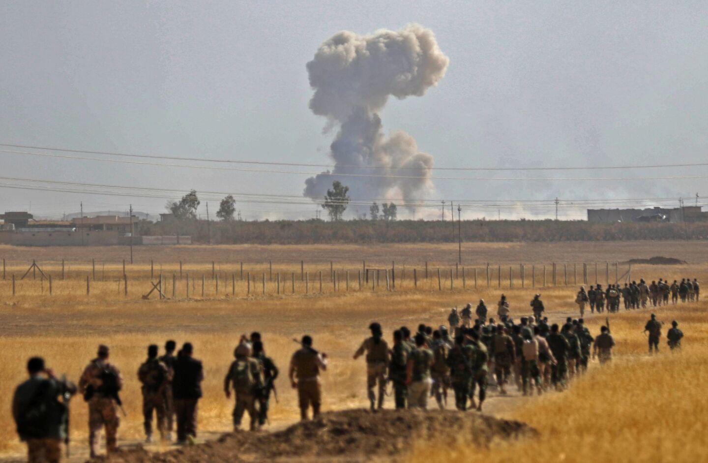 Smoke billows from an area near the Iraqi town of Nawaran, northeast of Mosul, as Iraqi Kurdish Peshmerga fighters march down a dirt road during the ongoing operation to retake the city from Islamic State.