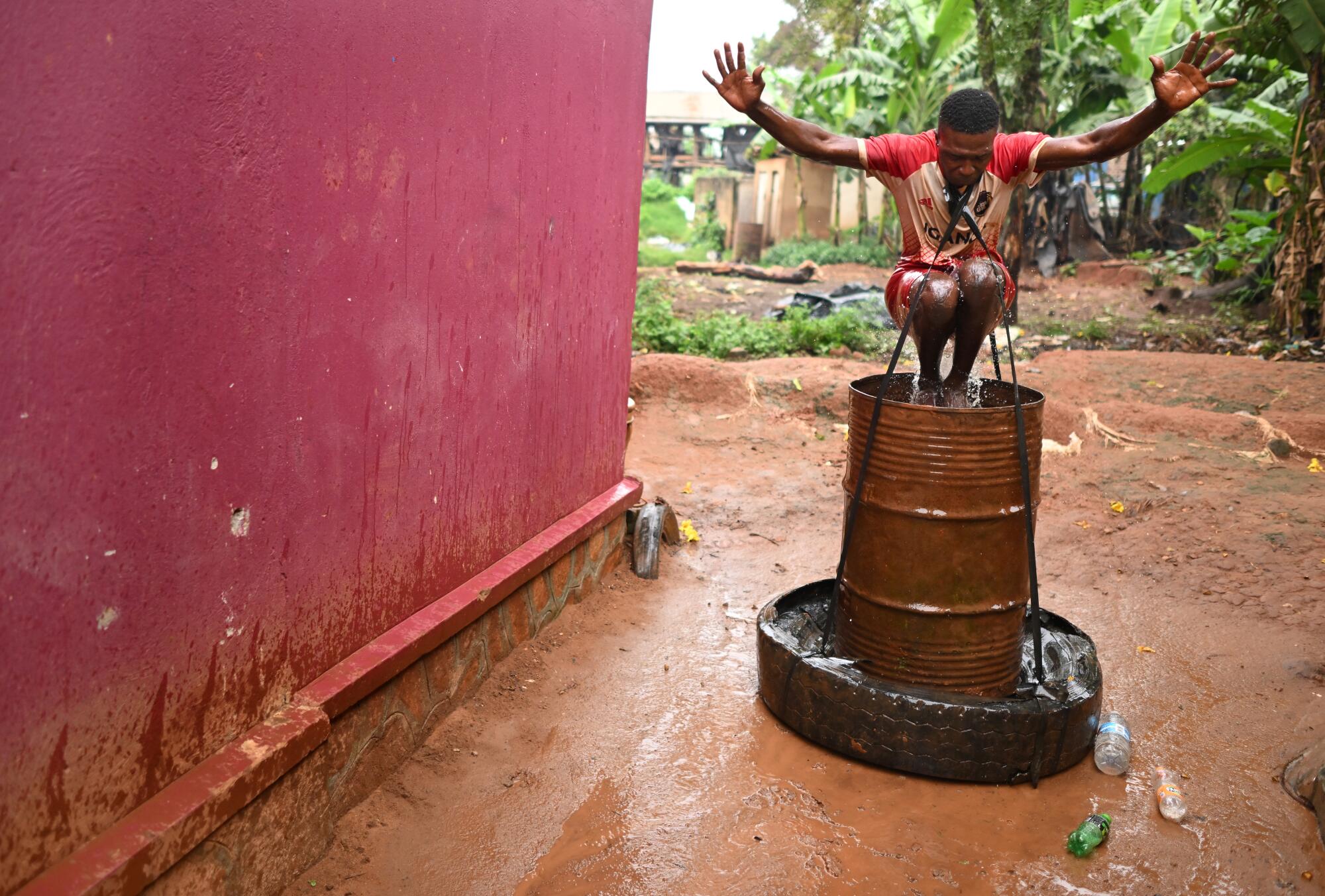 Dennis Kasumba jumps into a drum full of water to strengthen his legs outside his home in Uganda.