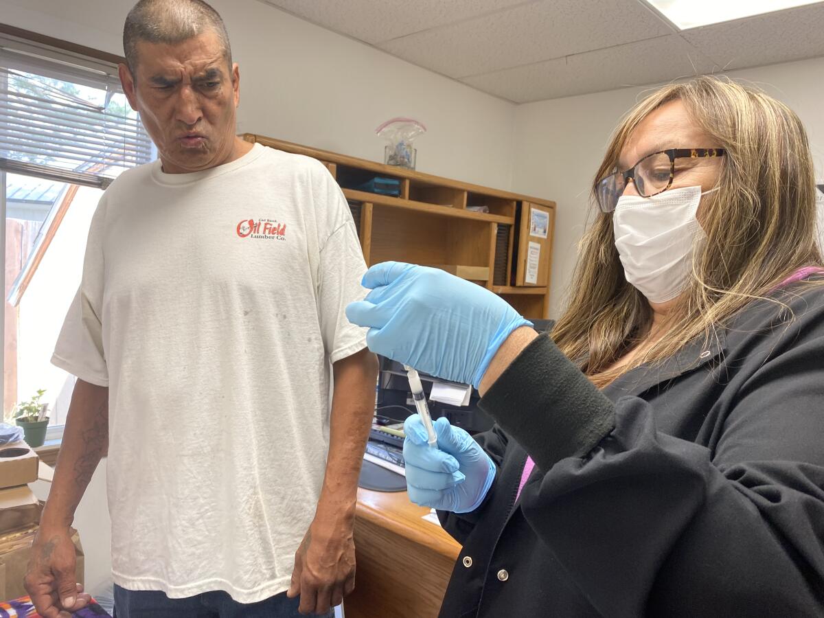 Man winces at vaccination needle being prepared by nurse.