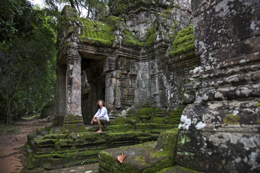 Cambodia - Young traveller, with curly hair, wearing a white long sleeve shirt and light shorts, visiting the ruins of Preah Khan in Angkor Wat
