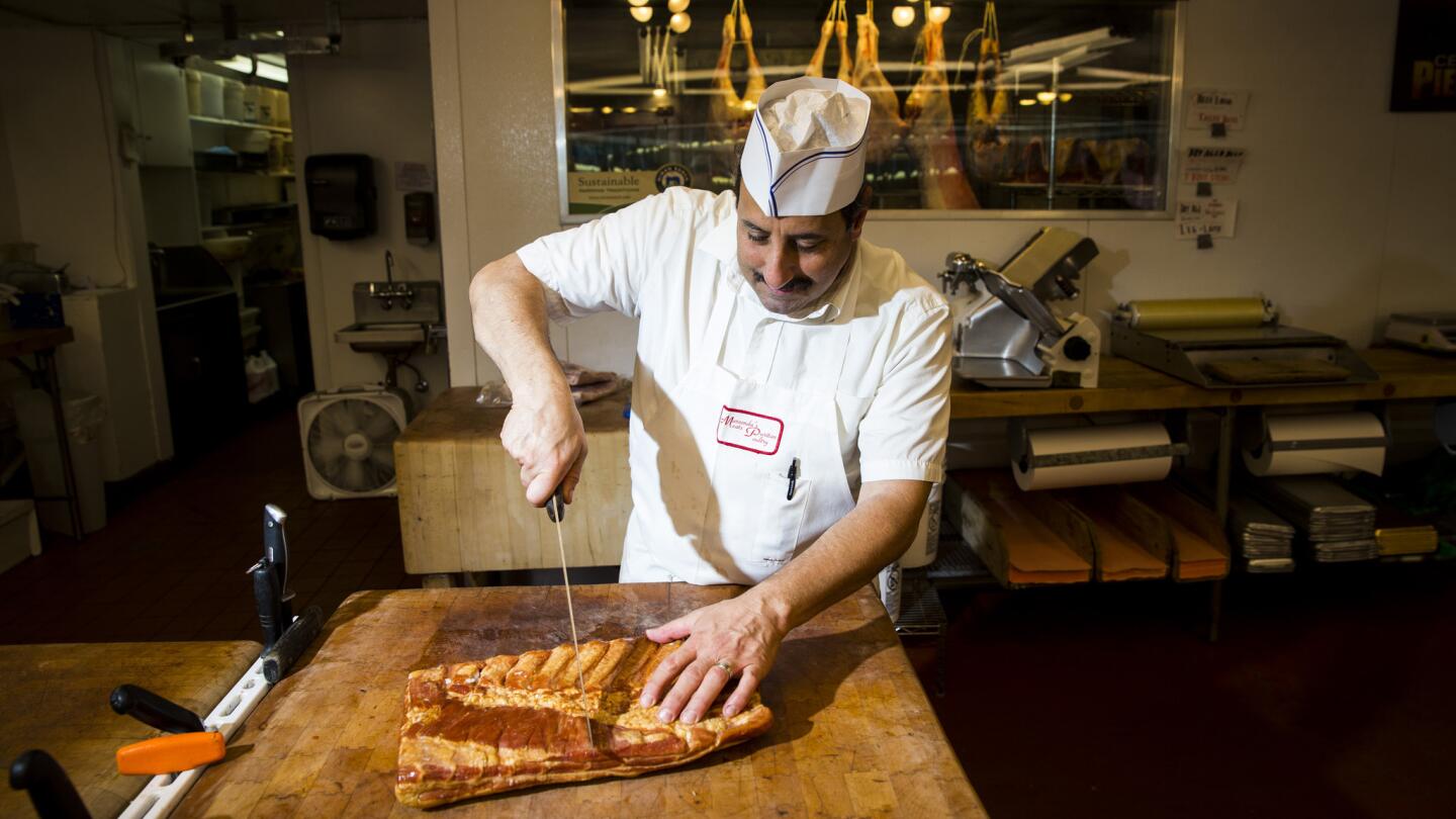 Butcher Lou DeRosa, whose family has run Marconda's Meats at the Los Angeles Farmer's Market since 1941, cuts a slab of Danish pork belly in half.