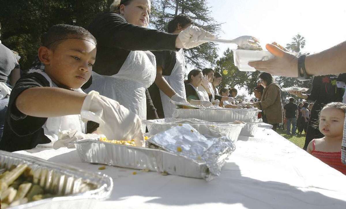 Kindrick Lino, 6, of Burbank, helps serve corn during last year's annual Thanksgiving meal at Central Park in Pasadena. Union Station Homeless Services is not accepting prepared food donations this year.