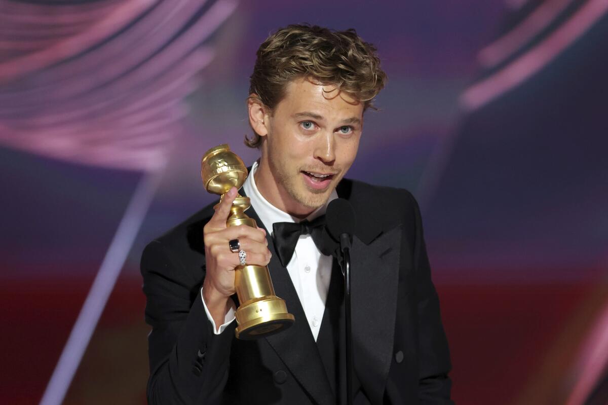 A young man in a tuxedo holding a golden award statuette