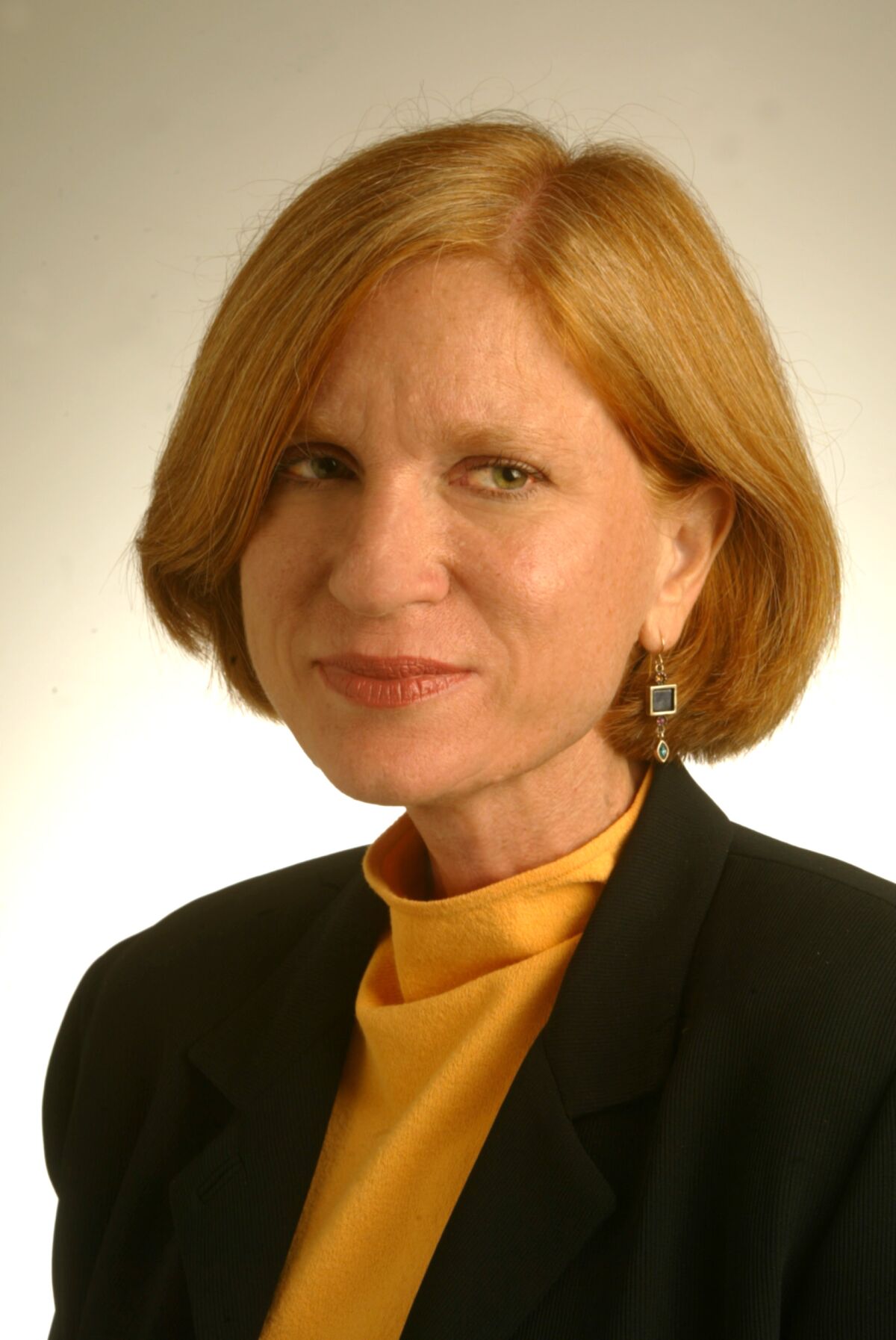 A headshot of a woman with a sleek bobbed haircut, in a blue blazer and high-neck gold shirt.