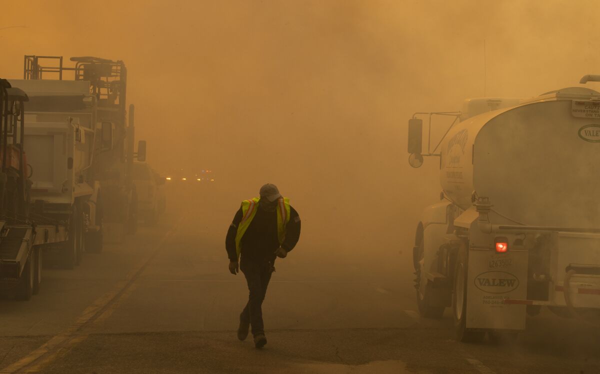 A water truck operator runs through the thick smoke of the advancing Silverado Fire fueled by Santa Ana winds at the 241.