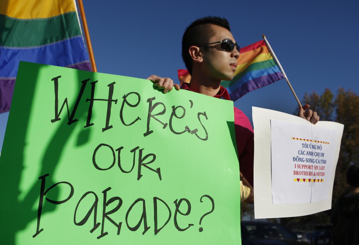 Minh Tran holds a sign and gay pride flag in Westminster last year as he protests the decision to exclude LGBT individuals from the 2013 Tet parade in Little Saigon.