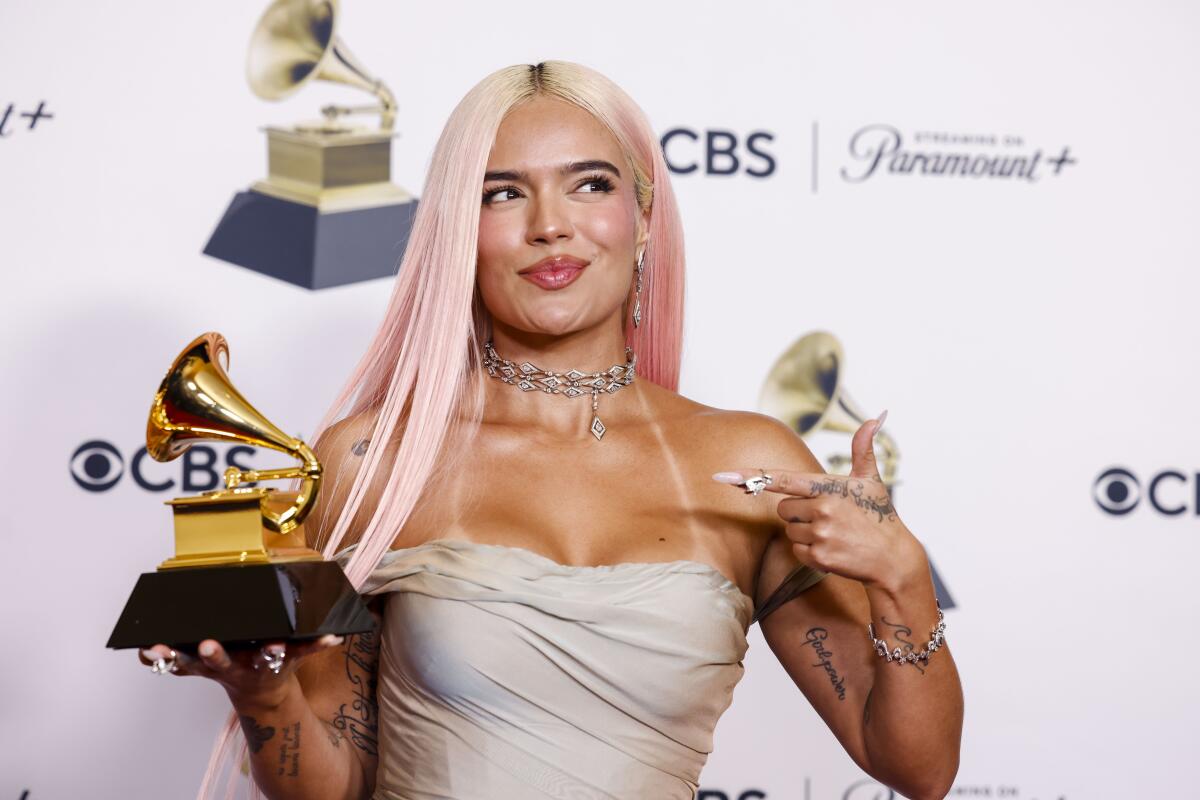 Karol G points at the Grammy she's holding in her right hand