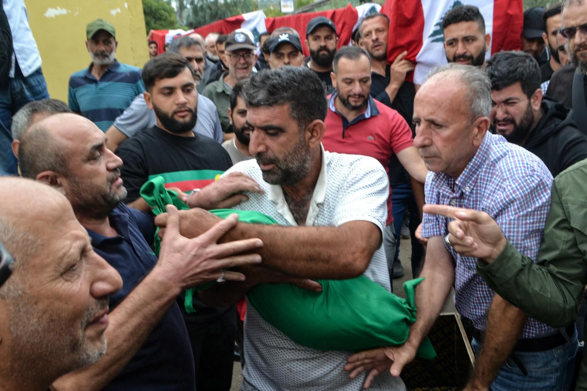 A man is surrounded by other men as he carries the shrouded body of a child.