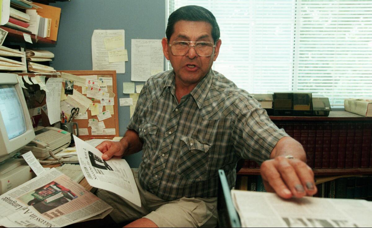 A man sitting at a home office desk reaches for a sheet of paper