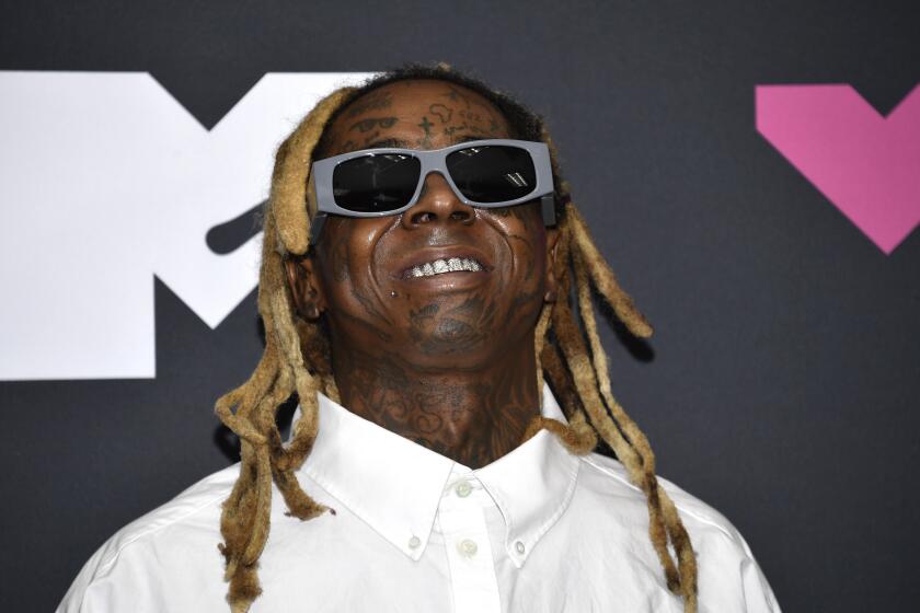 Lil Wayne wears large sunglasses and smiles with his signature locs