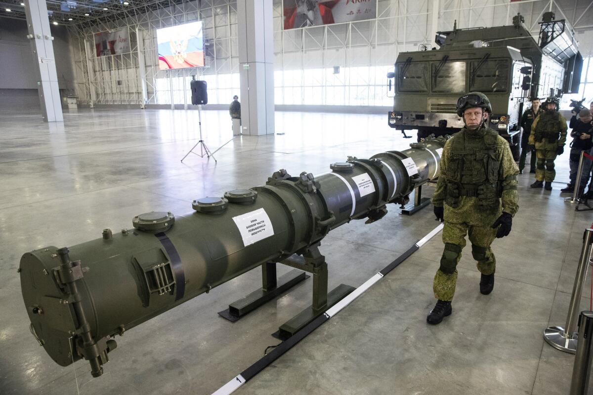 A Russian military officer walks past a 9M729 land-based cruise missile on display in a large building. 