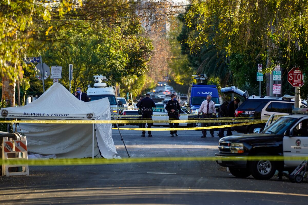 Yellow crime scene tape crosses a street where police officers are standing and a tent is set up. 