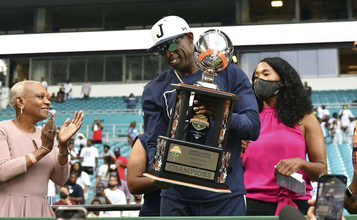 Jackson State head football coach Deion Sanders, center, holds the Orange Blossom Classic trophy after winning an NCAA college football game over Florida A&M, Sunday, Sept. 5, 2021, in Miami Gardens, Fla. (AP Photo/Jim Rassol)