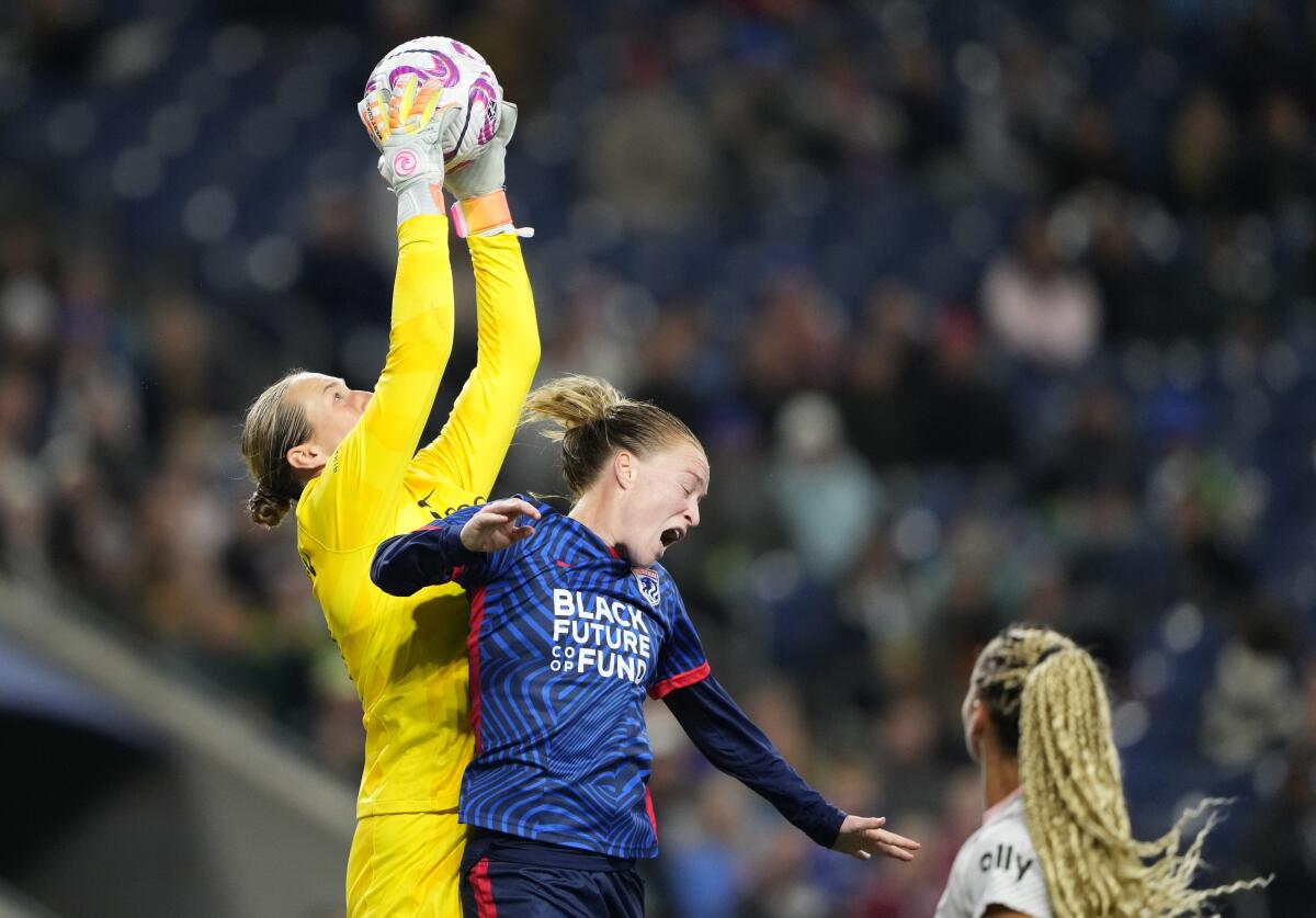 Angel City FC goalkeeper Angelina Anderson, left, reaches above OL Reign's Emily Sonnett to grab the ball.
