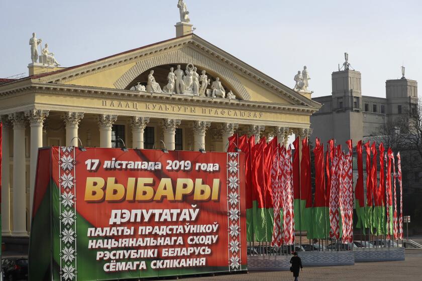 FILE - A woman walks past a huge election banner and Belarus national flags in Minsk, Belarus, on Nov. 13, 2019. Belarusians will cast ballots Sunday in tightly controlled parliamentary and local elections that are set to cement an authoritarian leader's rule, despite calls for a boycott by an opposition leader who described the balloting as a "senseless farce." (AP Photo, File)