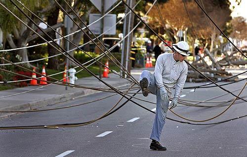 A Southern California Edison worker makes his way through downed power lines after winds toppled utility poles along Grand Avenue in Santa Ana.