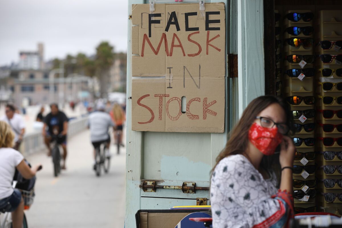 Woman in mask with "Face masks in stock" sign.