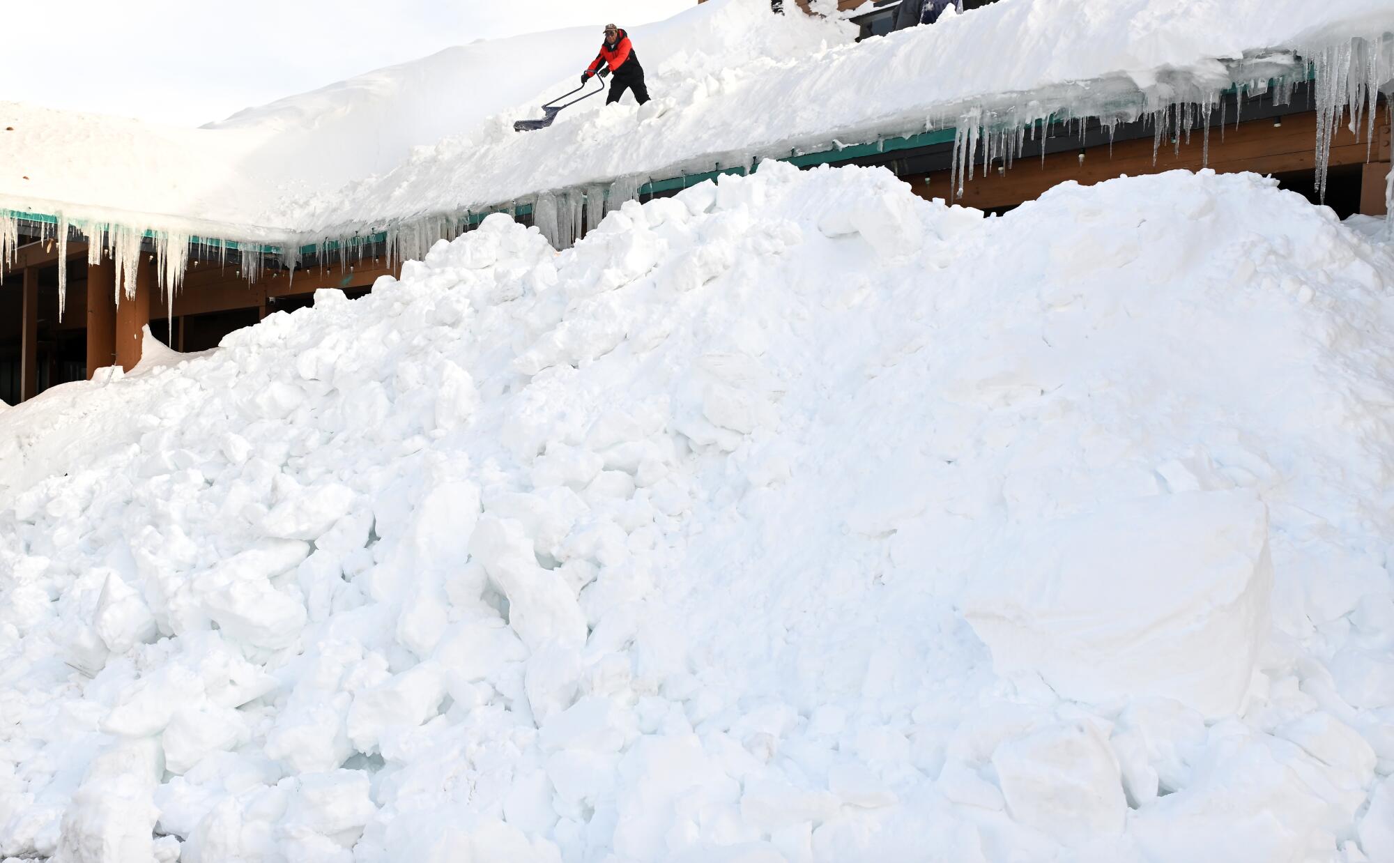 A worker is dwarfed as he shovels snow off a roof in Mammoth Lakes.