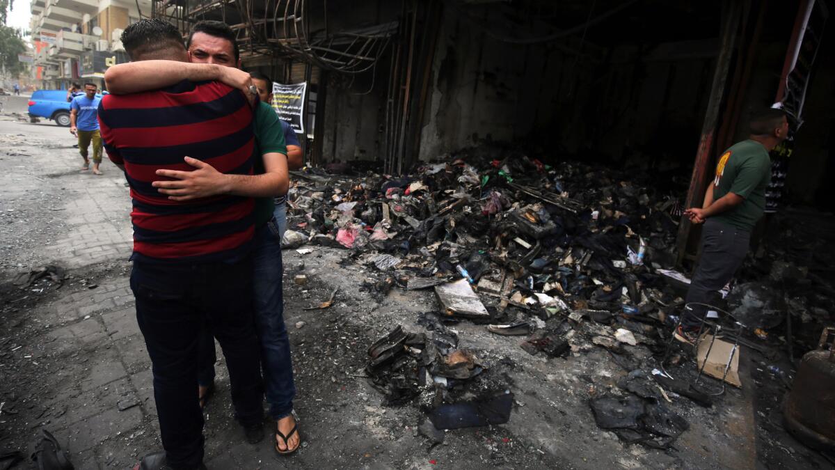 Iraqi men console each other on July 4, 2016, at the site of a suicide-bombing attack that took place a day earlier in Baghdad's Karada neighborhood.