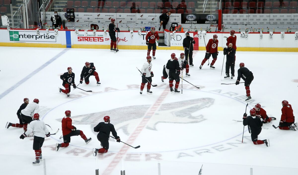 Arizona Coyotes players and coaches pause on the ice during practice in Glendale, Ariz.