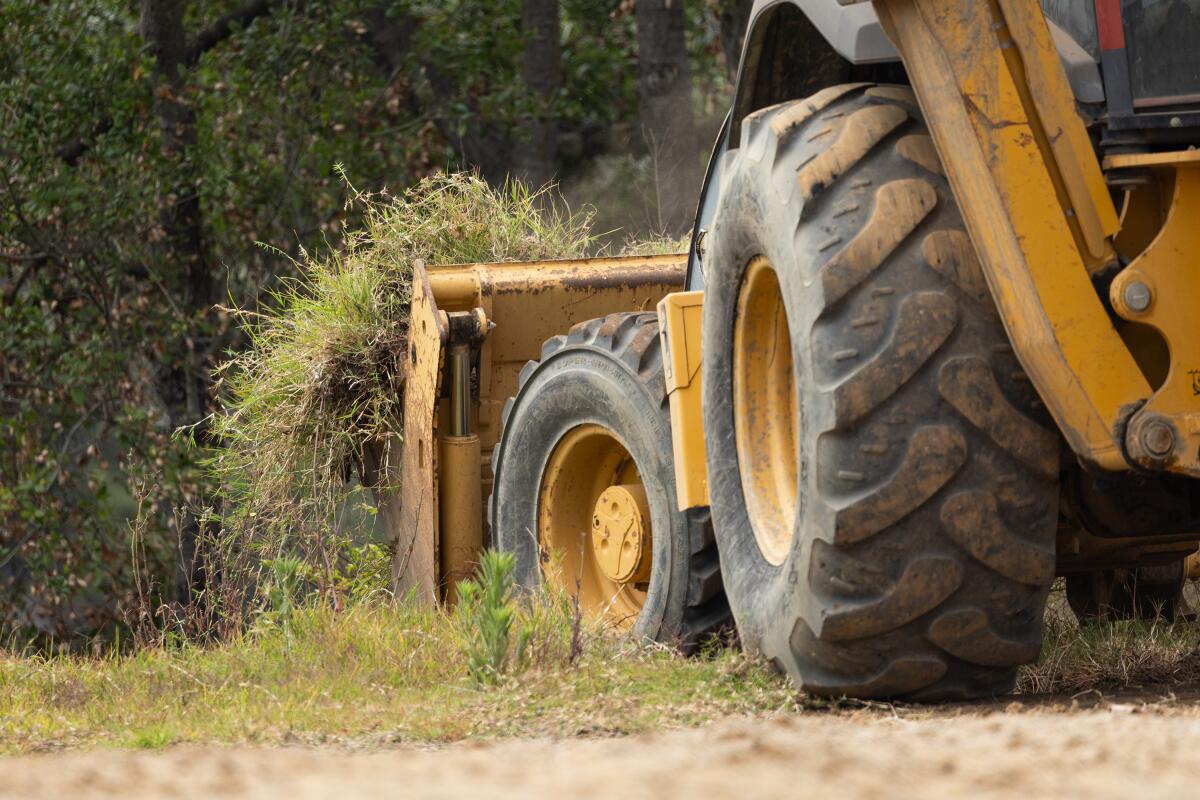 a backhoe scrapes dirt and grass