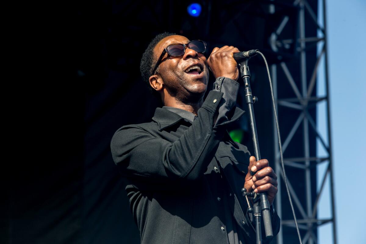 A Black man in sunglasses and a black suit sings into a microphone