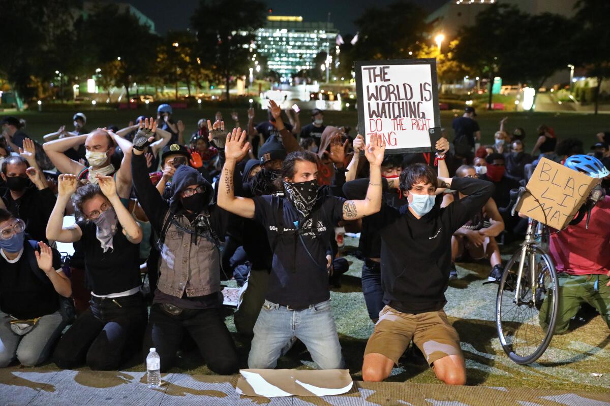 Protesters kneel and hold their hands in the air after dark at Grand Park in downtown Los Angeles