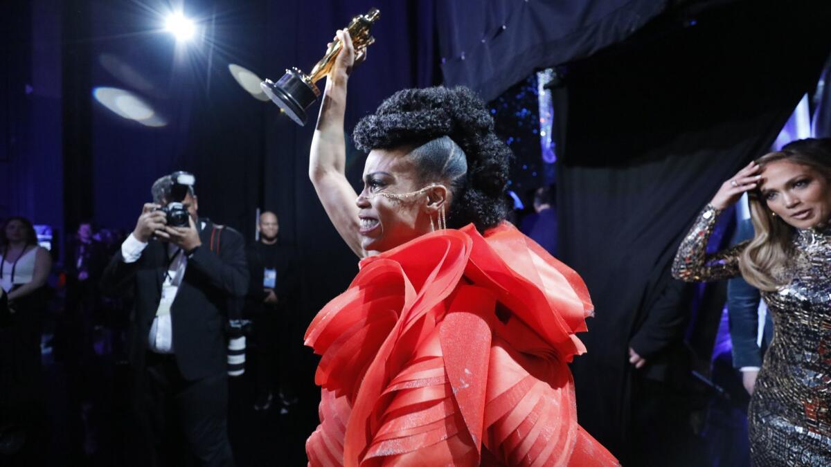 "Black Panther" production designer Hannah Beachler, the first African American woman to win in her category, holds her statuette aloft as J. Lo looks on.