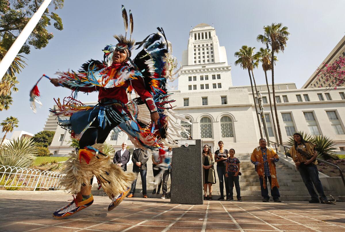 A Navajo Nation champion dancer in traditional dress dances in front of a government building.