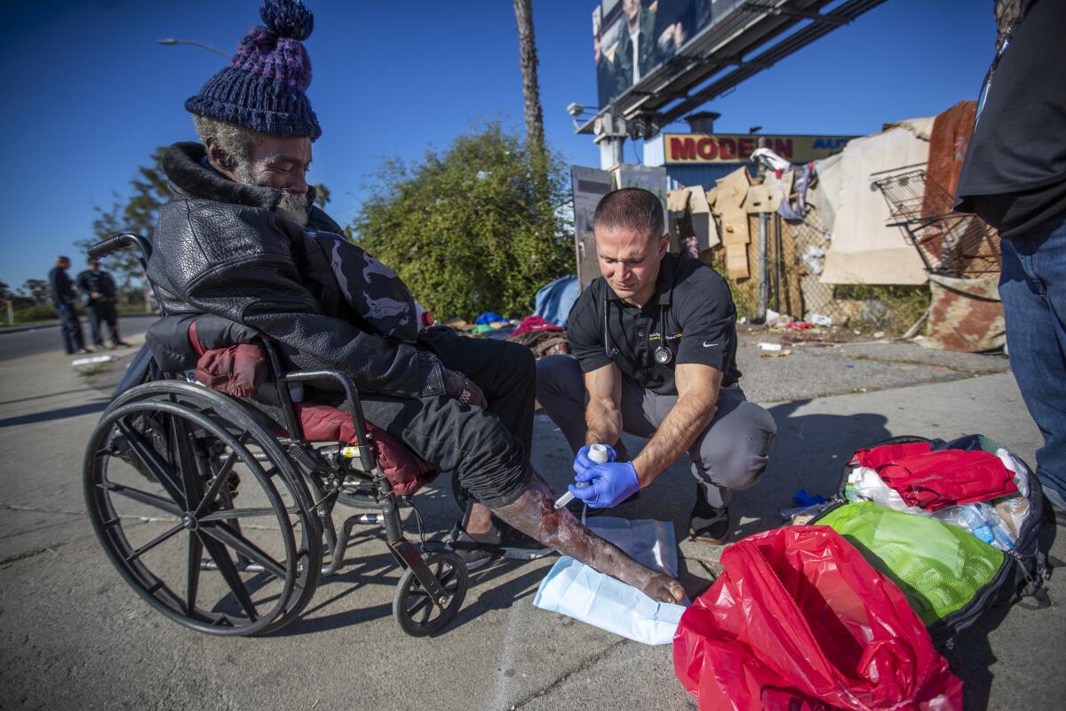 Brett Feldman treats the open wounds on the leg of homeless patient Alfred Mills, 62, at his encampment next to the 10 Freeway.