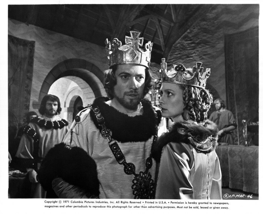 A man and a woman wearing large crowns in a black-and-white movie still.
