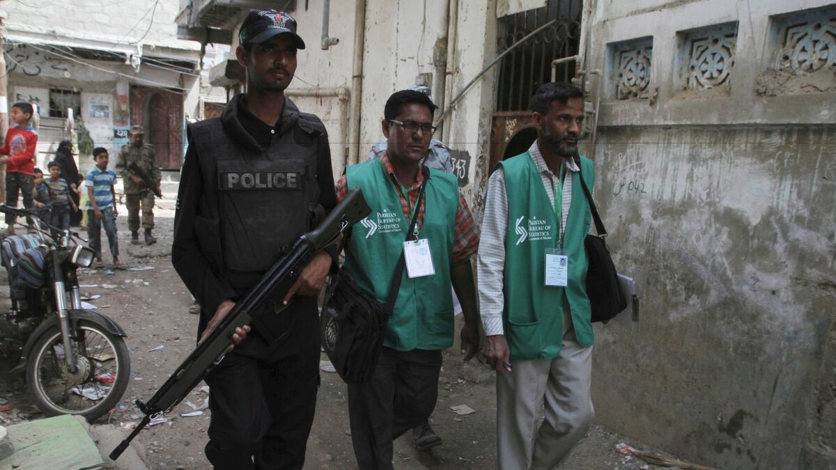 A police officer escorts government workers through the slums of Karachi, Pakistan, to collect data during the country's first census since 1988.