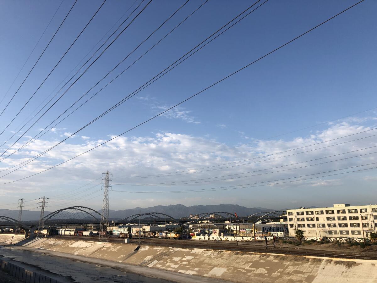 The arches of the 6th Street Bridge bound over the L.A. River and light industrial warehouses, with mountains as backdrop