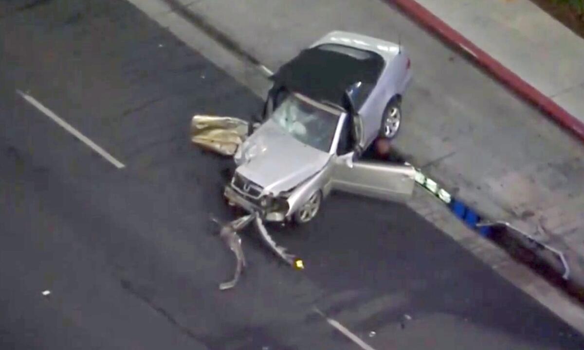 An aerial photo of wreckage of a silver car sitting partly off the street, on a median.