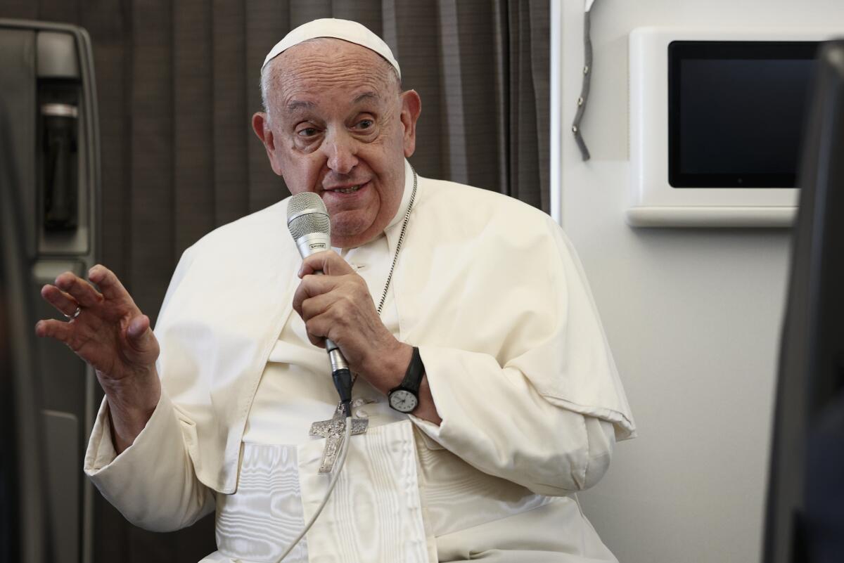 Pope Francis speaking into a microphone in his left hand and gesturing with his right hand