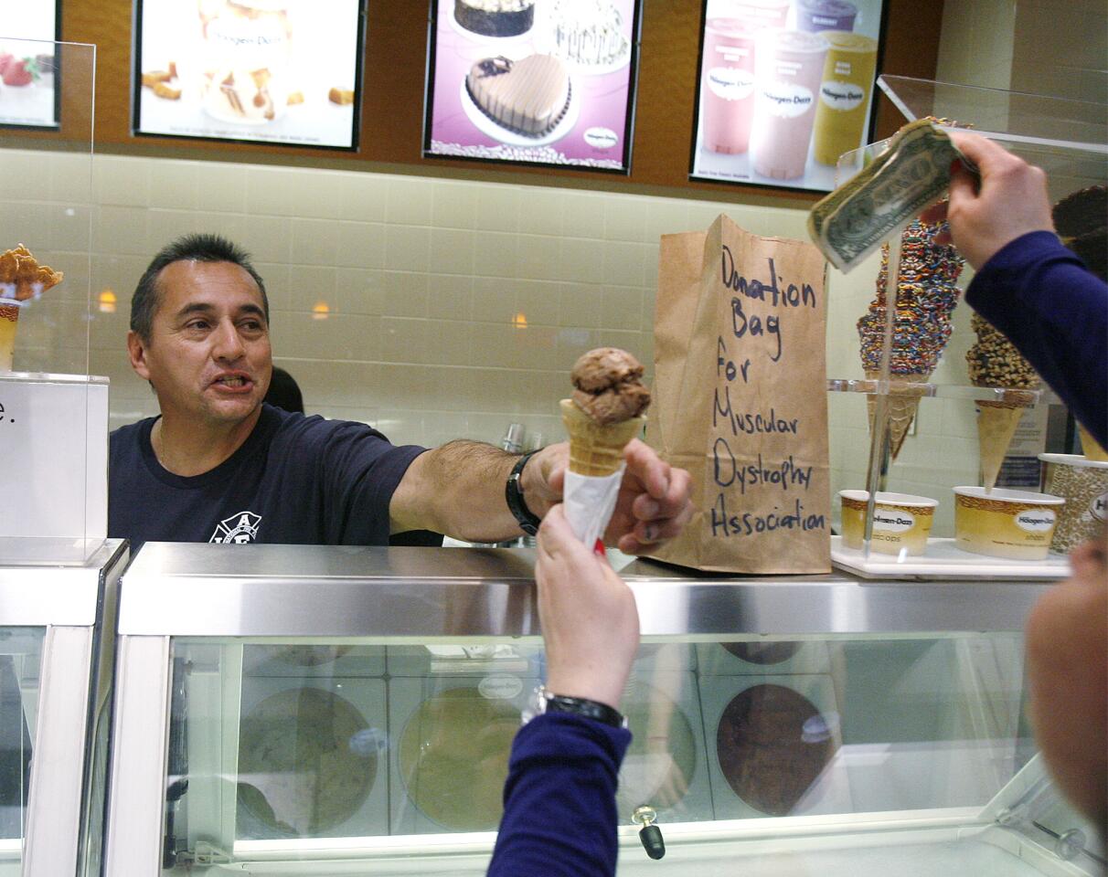 Firefighter/paramedic Ruben Mercado with the Burbank Fire Department smiles as he hands off a free ice cream cone as a donation is being placed in the bag at Haagen-Dazs in the Burbank Town Center on Tuesday, February 5, 2013. The firemen were giving out free scoops of ice cream and asking for donations to the Muscular Dystrophy Association.