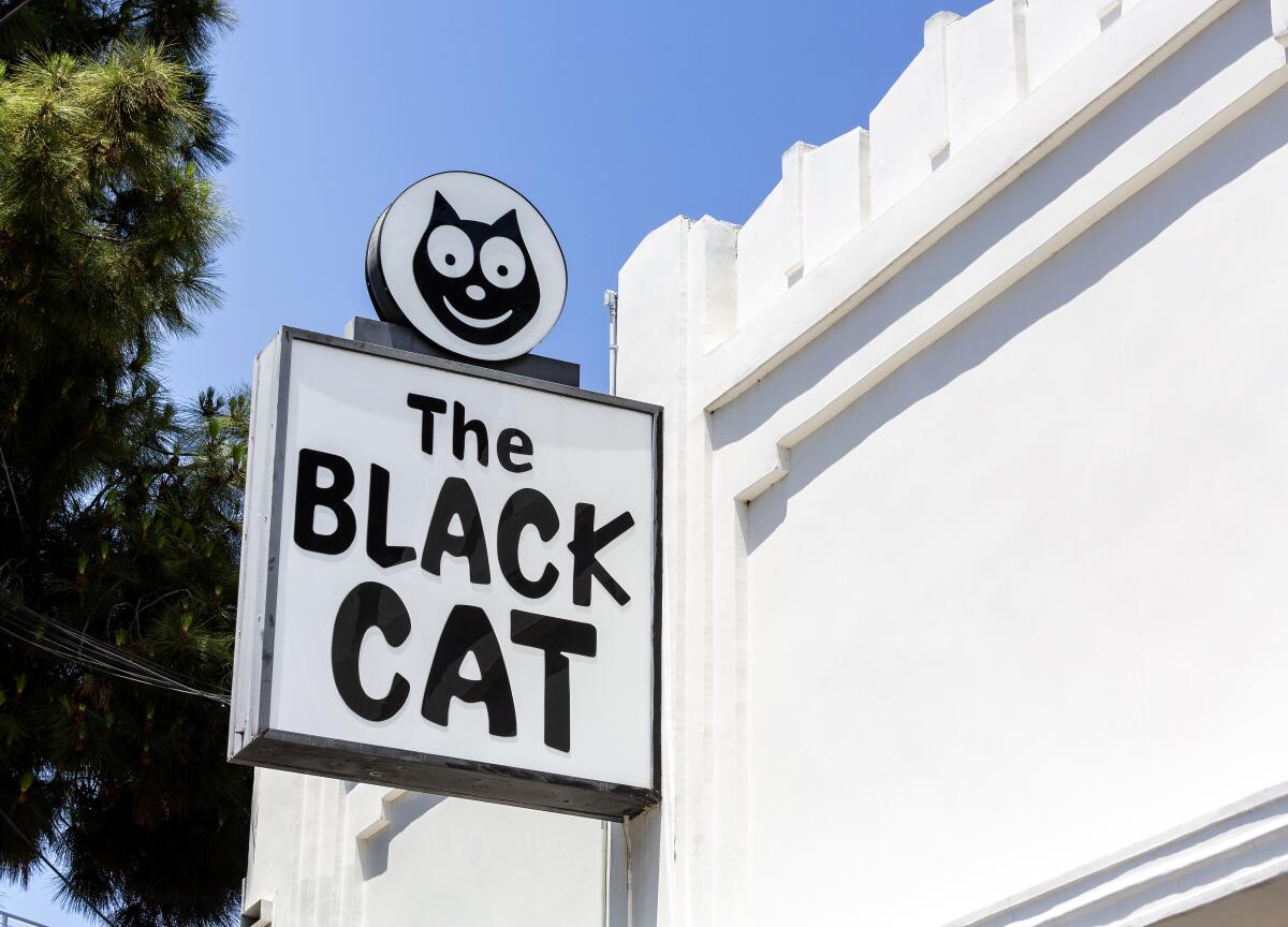 Closeup of a sign extending from a building that says "The Black Cat" and has a cartoon image of a cat's face.