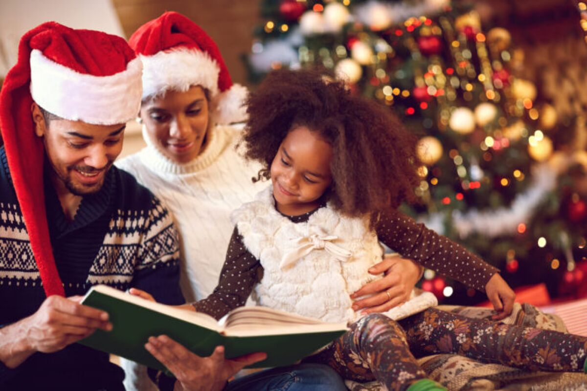 smiling mother, father and daughter read a book at fireplace on Christmas