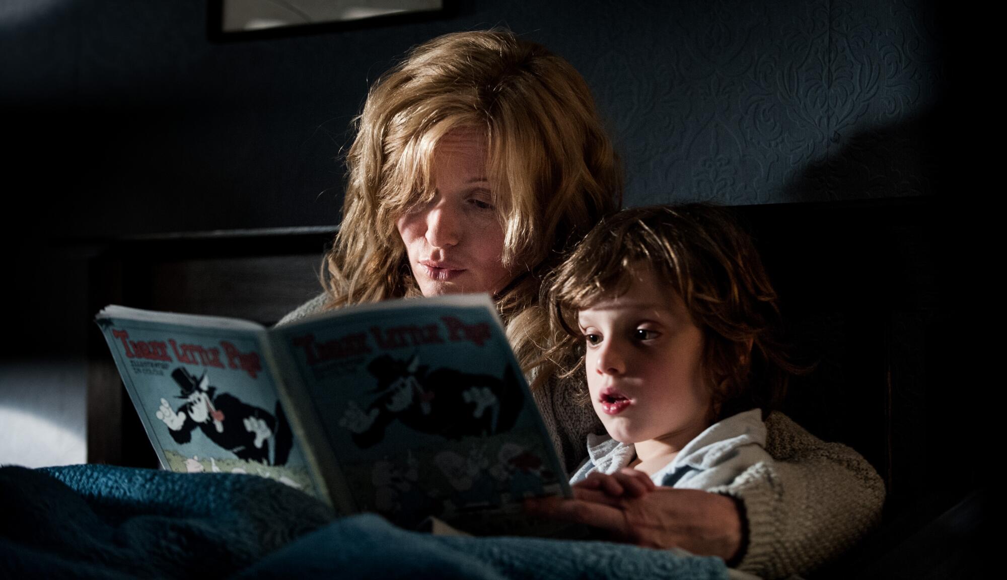 A mother reads a book to her son in bed.