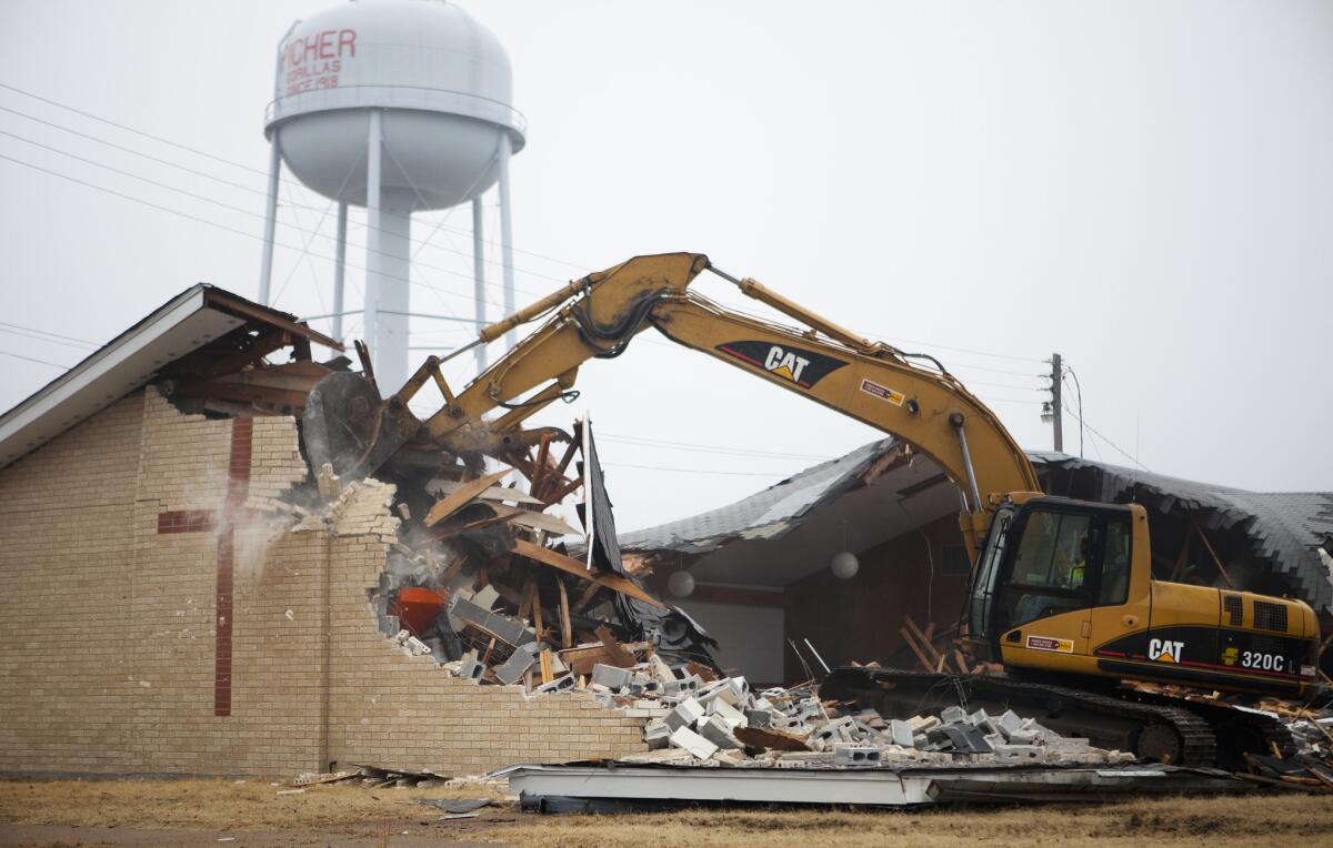 With the town's water tower looming behind, an excavator takes methodical swings at the First Baptist Church of Picher, Okla., quickly demolishing it into a pile of rubble.
