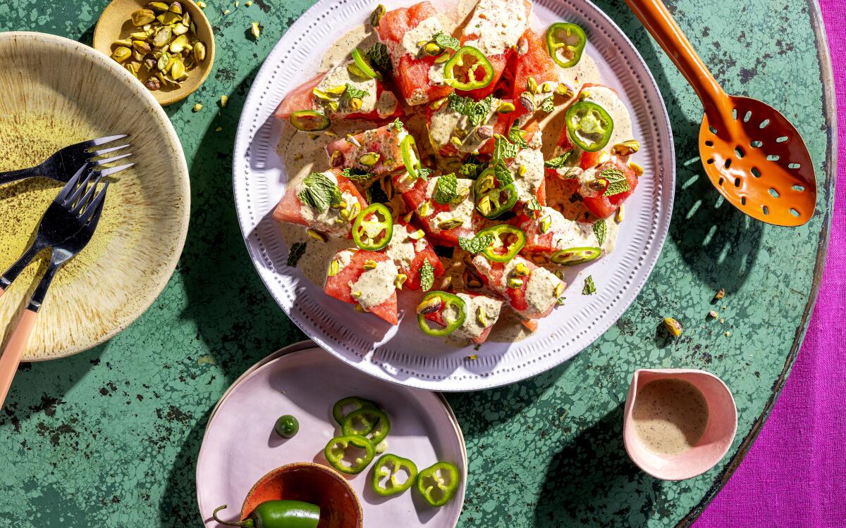 A salad of spiced chunks of watermelon drizzled with dressing, topped with sliced chiles and pistachios on a plate