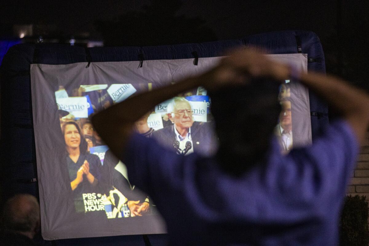 A community activist watches Sen. Bernie Sanders speak on screen