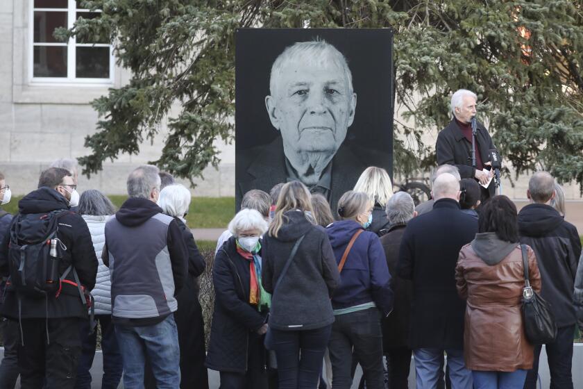 Participants of a memorial service for Buchenwald survivor Boris Romantschenko stand in front of his photo in Weimar, Germany Tuesday, March 22, 2022. Germany’s parliament has paid tribute to Boris Romanchenko, who survived several Nazi concentration camps during World War II but was killed last week during an attack in the Ukrainian city of Kharkiv. He was 96. (Bodo Schackow/dpa via AP)