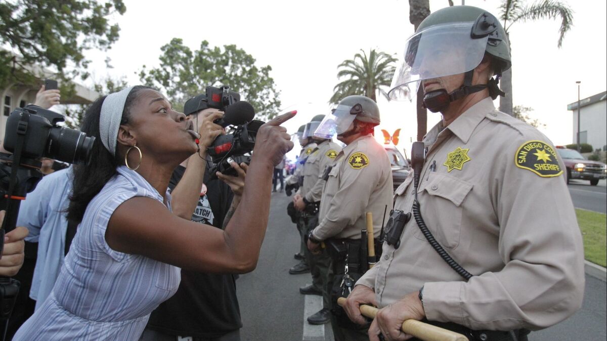 Rashida Hameed yells at a San Diego Sheriff's deputy while he and other deputies in riot gear stand in a line outside the National City council chambers where protesters demanded answers about the death of Earl McNeil in May.