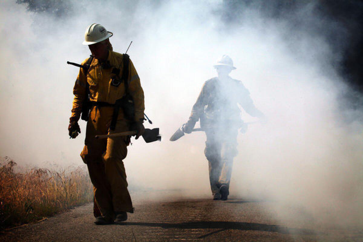 Firemen walk with shovels out of a wall of smoke after digging ditches to try to slow down brush fire in Monrovia.