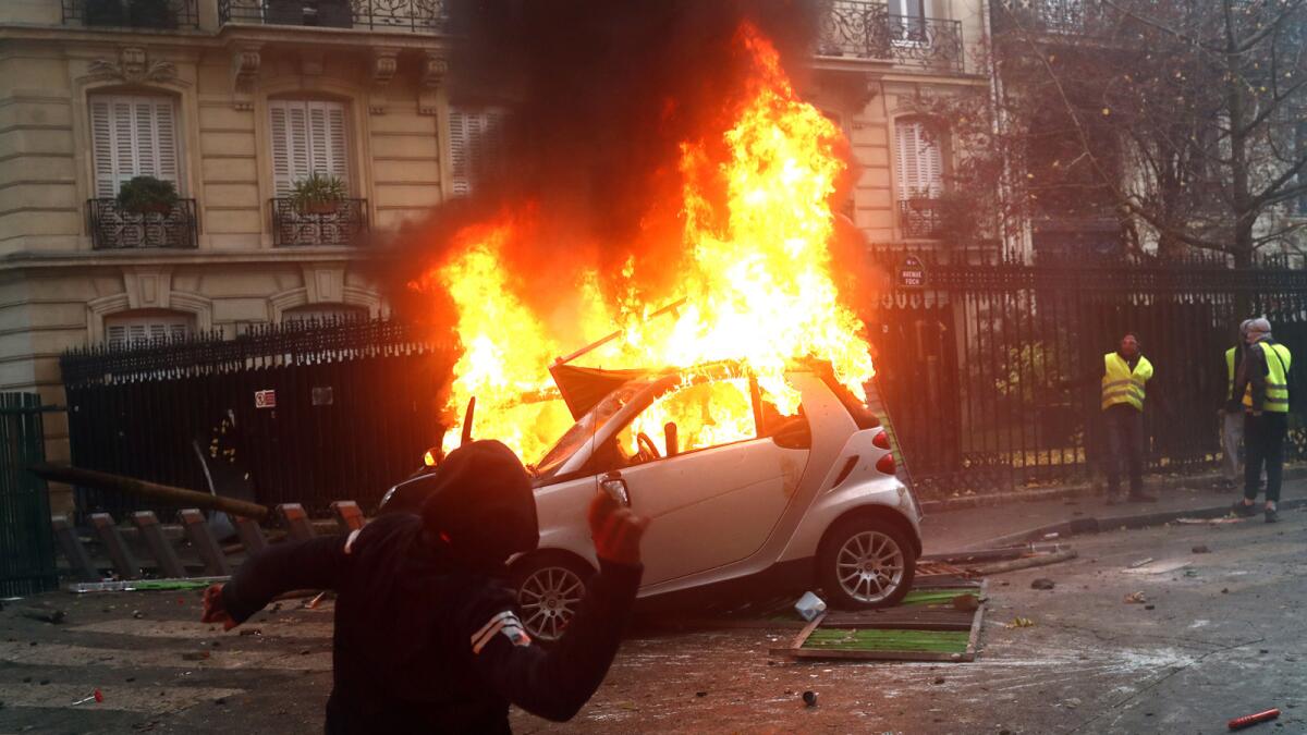 A hooded demonstrator throws something as a car burns Saturday during a protest in Paris.